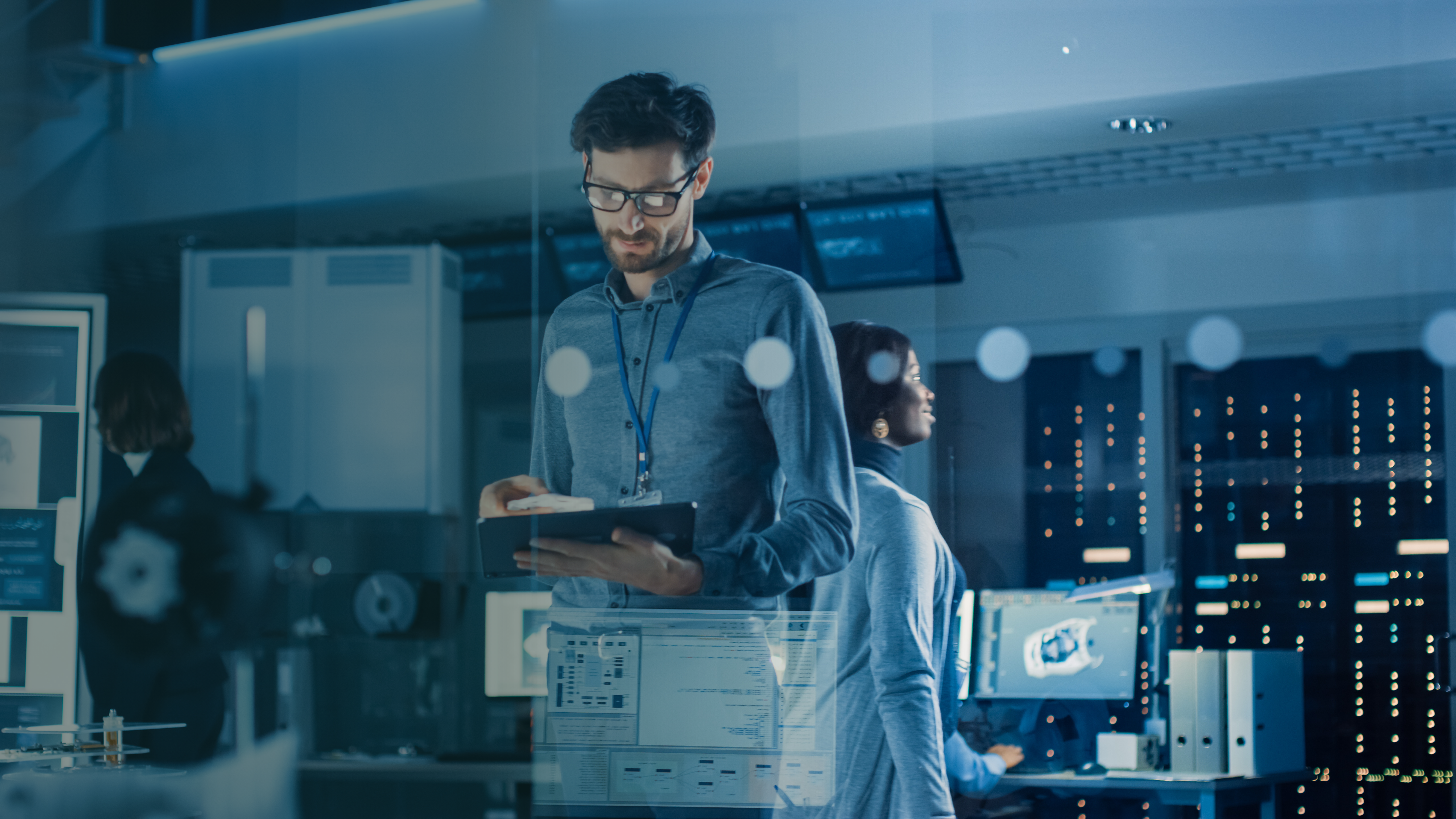 In Technology Research Facility: Chief Engineer Stands in the Middle of Lab and Uses Tablet Computer. Team of Industrial Engineers, Developers Work on Engine Design Use Digital Whiteboard and Computer